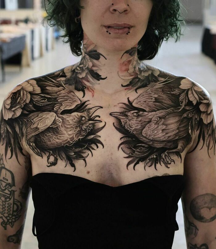 Person with intricate gothic tattoos featuring birds and floral designs on chest and arms.