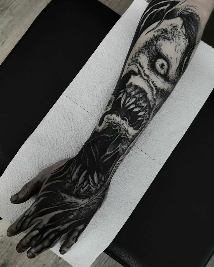 Intricate gothic tattoo featuring a menacing creature design covering an entire arm, showcasing dark artistry.