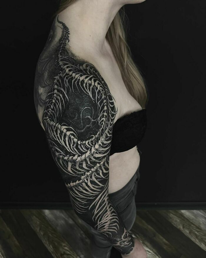 Gothic tattoo sleeve featuring intricate bone design on a woman's arm, set against a dark background.