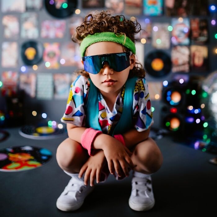 Child with Cheddar Wiz mullet hairstyle wearing colorful retro clothes and sunglasses in a vibrant music-themed room