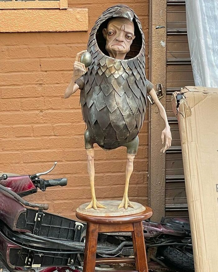 Metal sculpture with bird-like body and human face, one hand holding an egg, found among thrown out treasures in NYC.