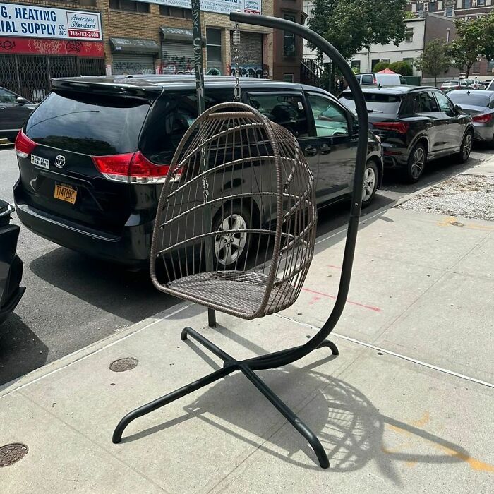 Wicker hanging chair with metal frame left on a NYC sidewalk, an example of real treasures discarded in the city.