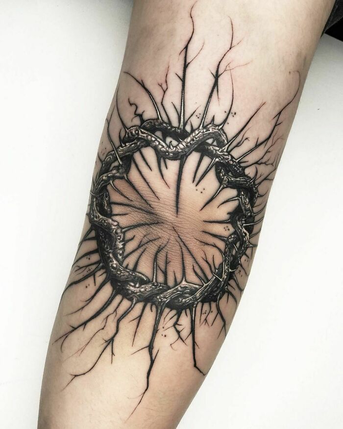 A detailed Gothic tattoo featuring an intricate, circular design with sharp, branching elements on forearm.