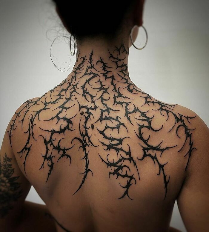 Back adorned with intricate gothic tattoos featuring thorn-like patterns.