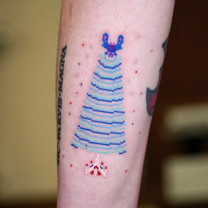 Pixelated Galaga video game tattoo with spaceship and alien design on arm.