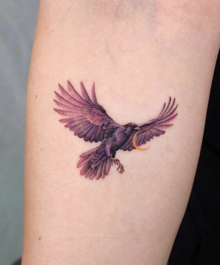 Gothic tattoo of a blackbird with open wings on an arm, showcasing intricate detail and a mysterious vibe.