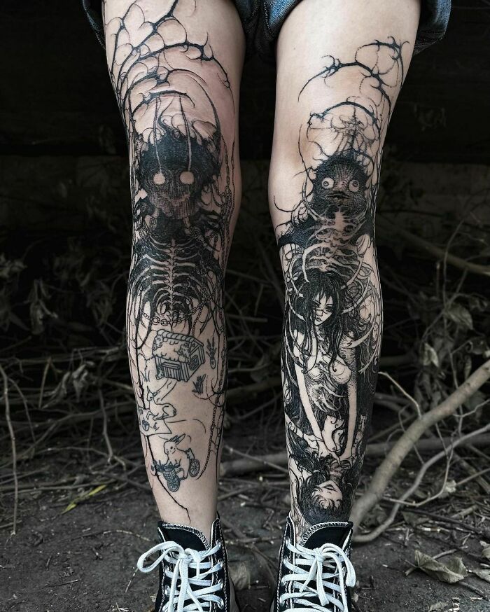 Intricate gothic tattoos on legs with black ink designs, featuring skeletal and surreal elements.