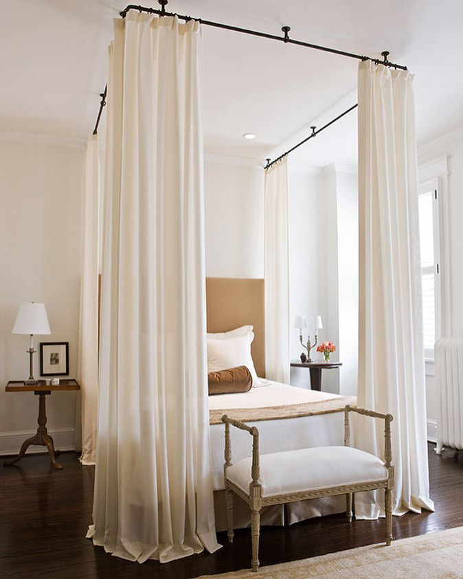 Large beige ceiling-to-floor curtains that hang around the bed and puddle up on the floor Large beige ceiling-to-floor curtains that hang around the bed and puddle up on the floor