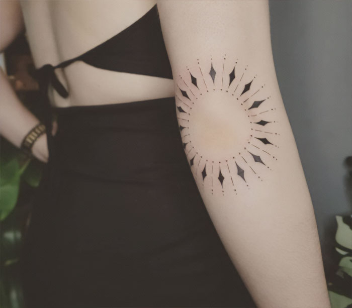 Unique geometric elbow tattoo design featuring a sunburst pattern on the arm.