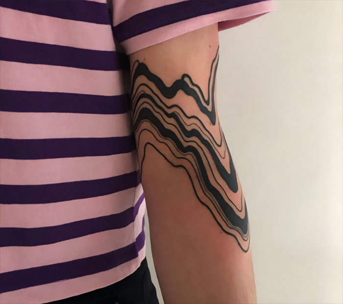 Abstract black line elbow tattoo design on a person wearing a pink and purple striped shirt.