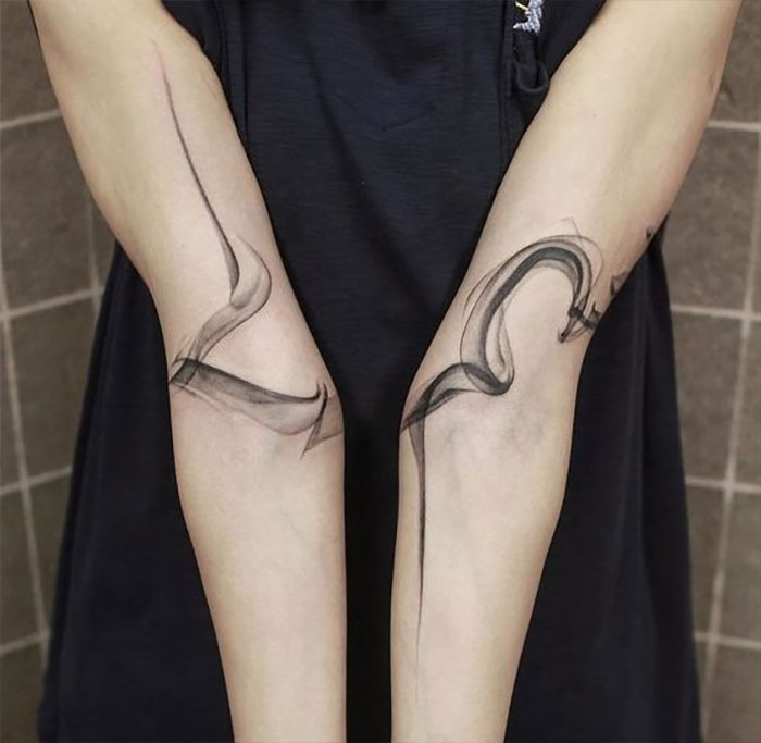 Abstract elbow tattoo design in black ink on forearms.
