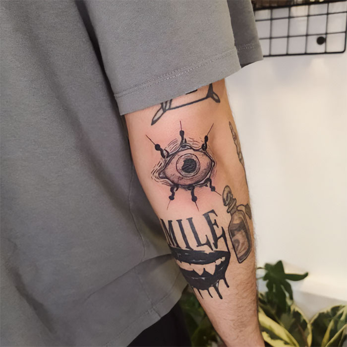 Close-up of eye-themed elbow tattoo on arm in a grey shirt.