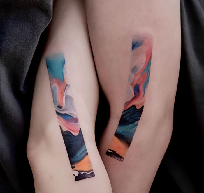 Abstract colorful elbow tattoos with vibrant swirling designs.