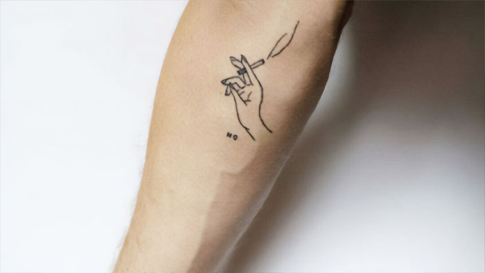 Minimalist elbow tattoo of a hand holding a cigarette on an arm.