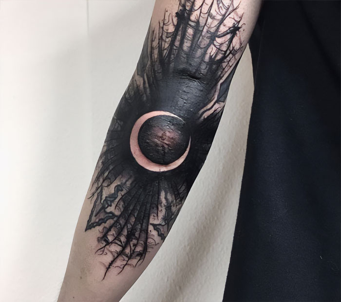 Abstract elbow tattoo featuring a black and white solar eclipse design.