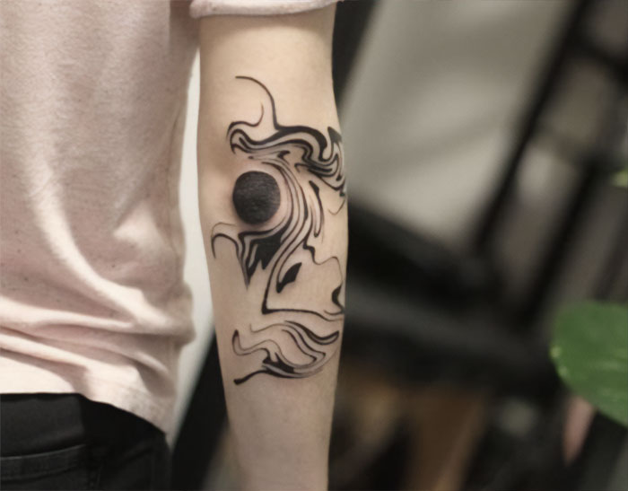 Abstract black ink design on elbow tattoo, featuring flowing lines and circular patterns.