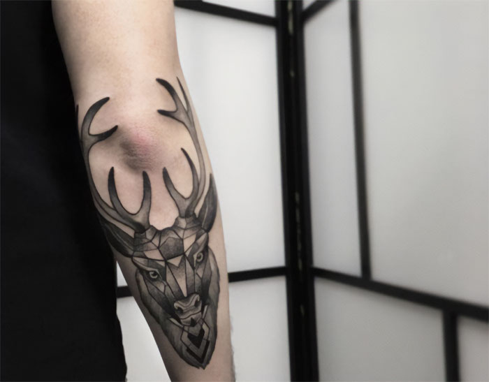 Geometric deer design on elbow tattoo, showcasing bold antlers and intricate details.