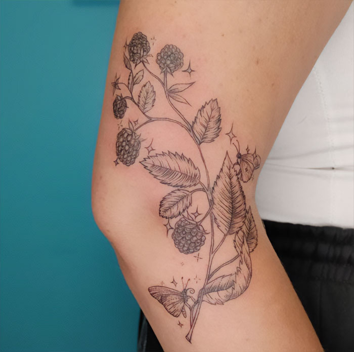 Floral elbow tattoo featuring blackberries and leaves, with intricate detailing and a butterfly design.