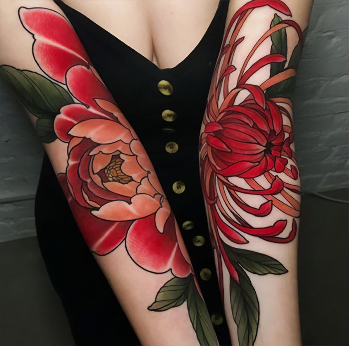 Colorful floral elbow tattoo designs on both arms against a dark dress background.