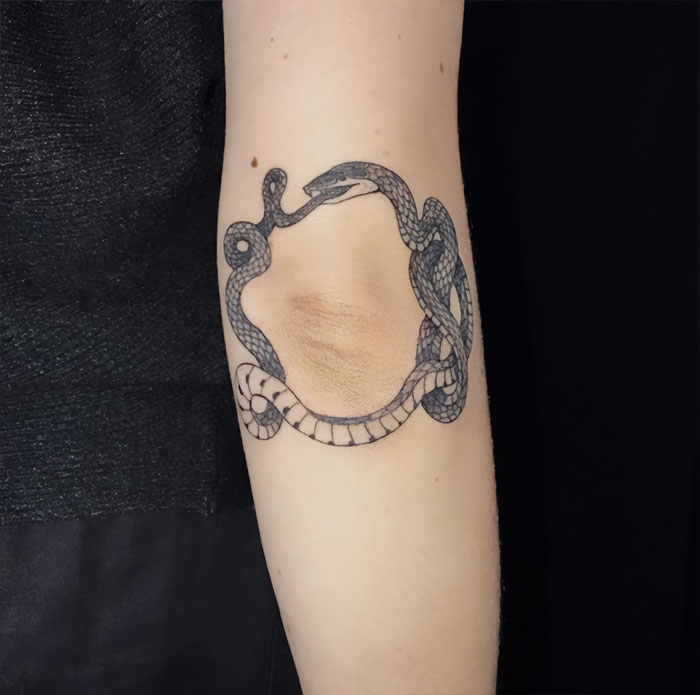 Snake tattoo coiled around an elbow, showcasing intricate design and detail for an elbow tattoo idea.