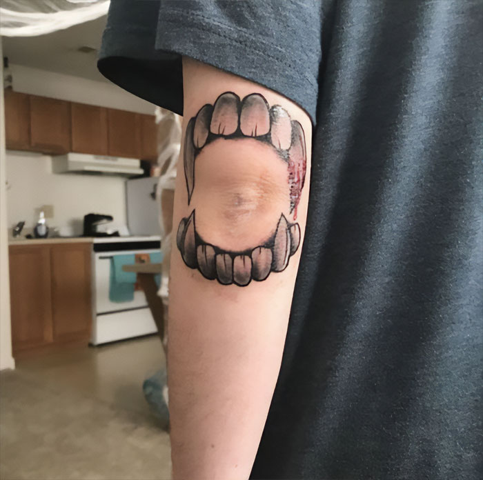 Elbow tattoo featuring realistic fanged mouth design, showcasing unique body art creativity.