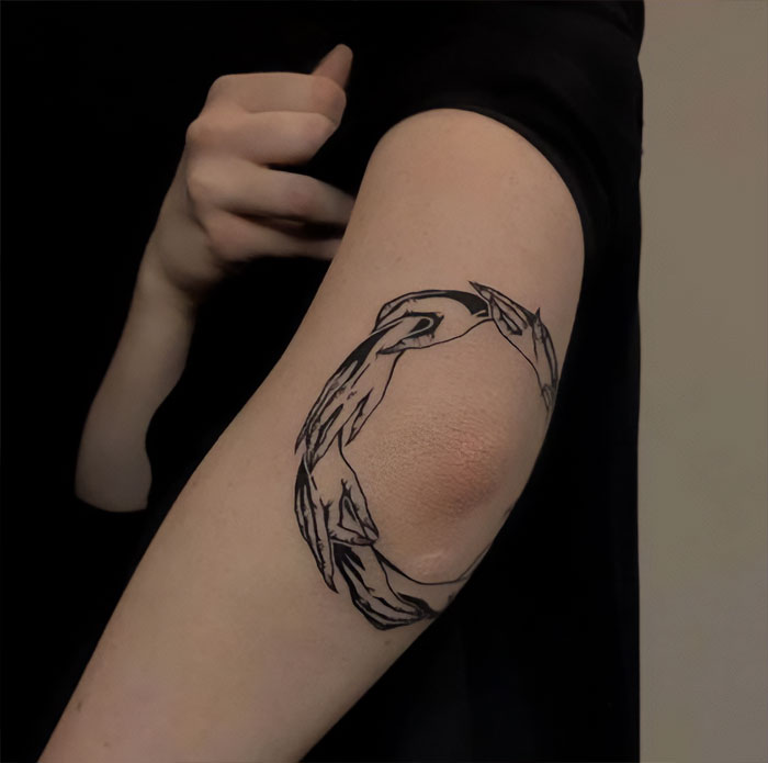 Elbow tattoo featuring a circular design of interlocking hands on a person's arm.