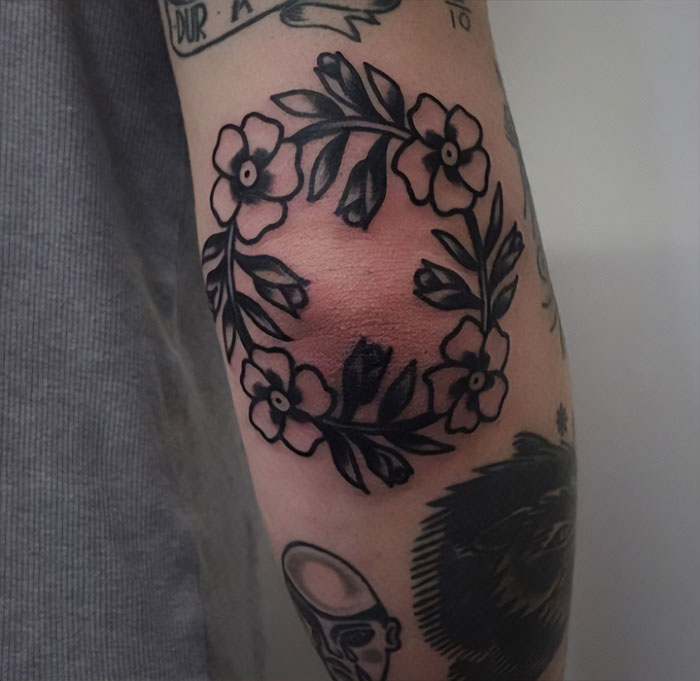 Floral elbow tattoo design with black ink outlines and leaves on an arm.