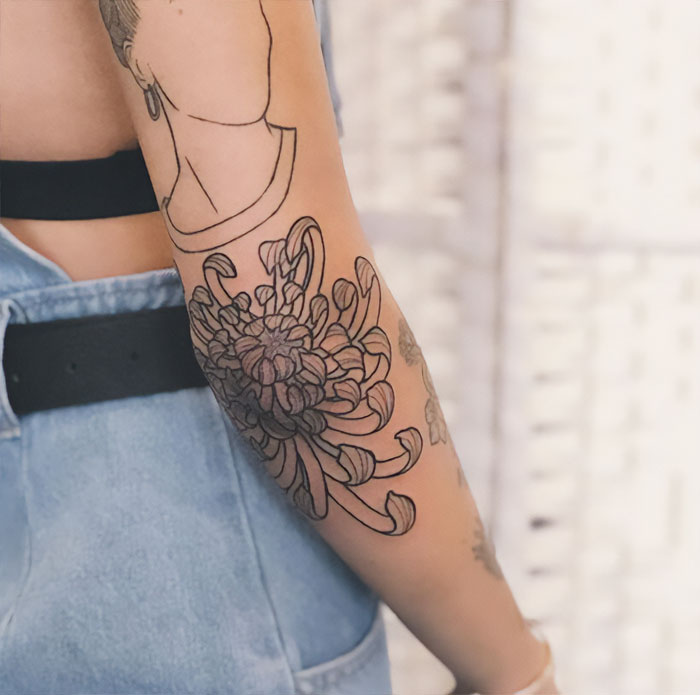 Floral elbow tattoo on a person's arm, styled with intricate linework and dress in denim attire.