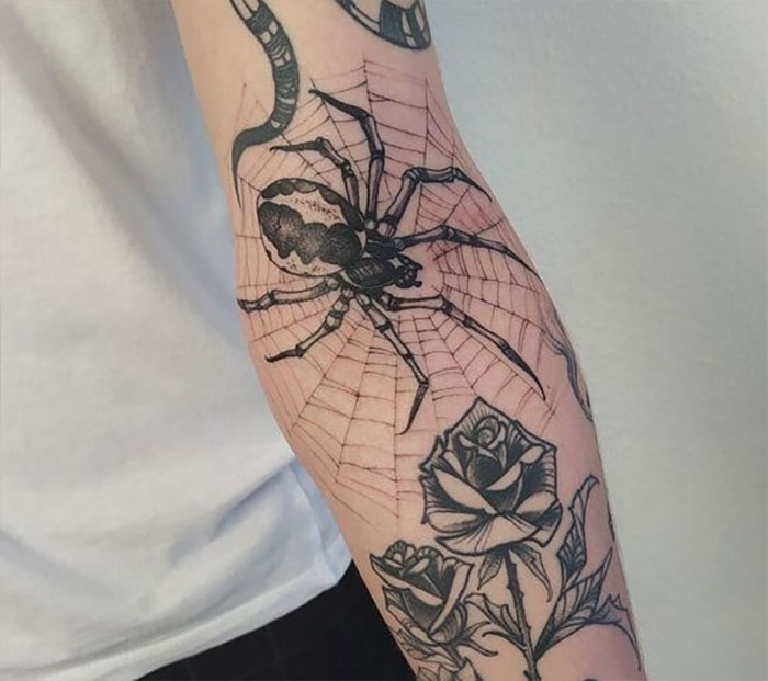 Spider and web tattoo design on elbow with rose details, showcasing a unique elbow tattoo idea.