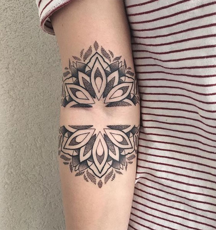 Geometric floral elbow tattoo design on a person's arm against a wall background.