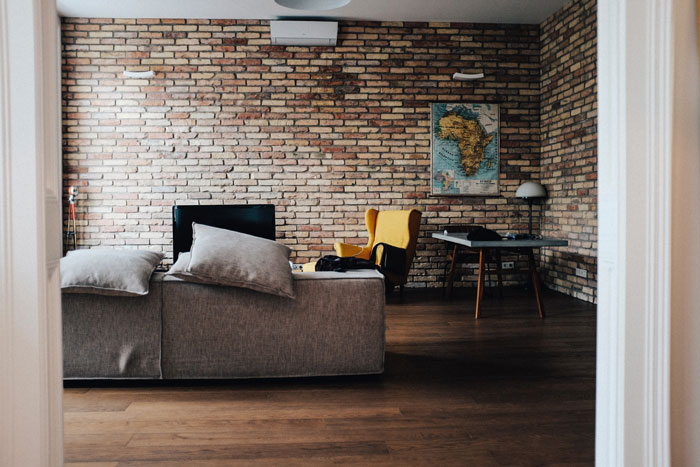 Rustic bricks wall in a room with gray couch and gray wooden table beside wing chair Rustic bricks wall in a room with gray couch and gray wooden table beside wing chair