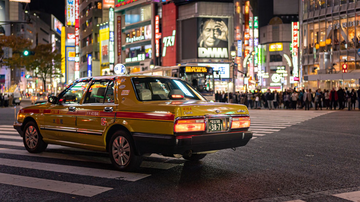 Yellow sedan taxi stopped at a busy Tokyo street crosswalk at night, showcasing culture facts reflecting diversity and beauty.