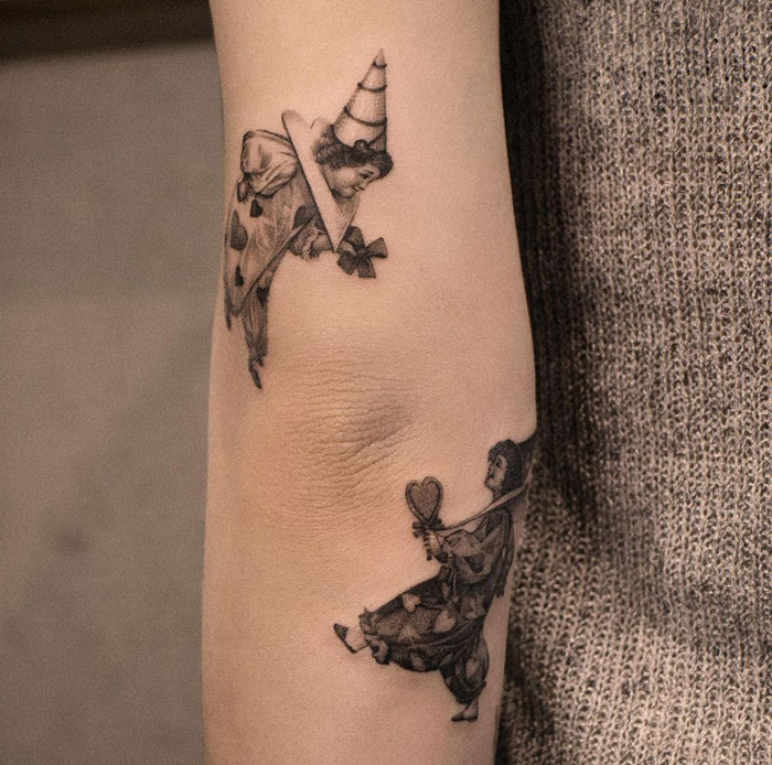 Clown-themed elbow tattoo in black and gray ink on a forearm.