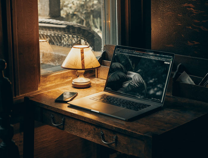 macbook pro on brown wooden table and lighted lamp macbook pro on brown wooden table and lighted lamp