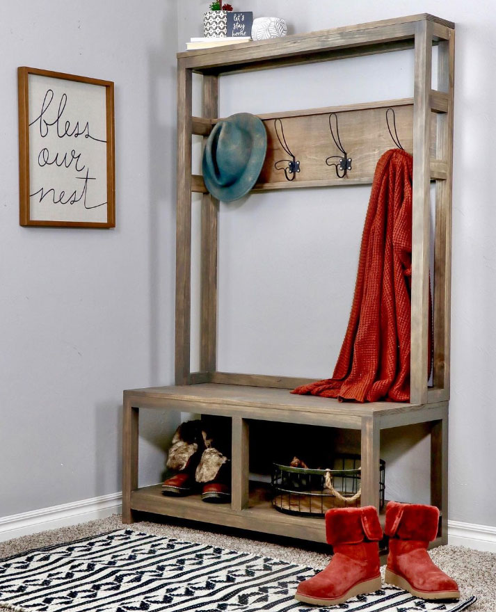 A wooden hall tree with a red hat and sweater on it and boots below A wooden hall tree with a red hat and sweater on it and boots below