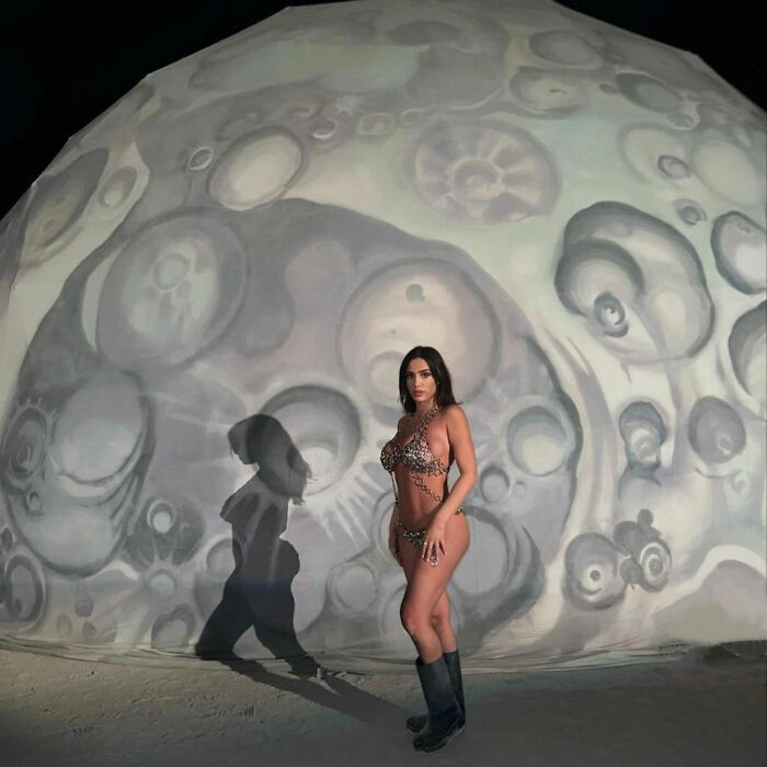 Bianca Censori in revealing outfit, standing in front of an abstract circular background.