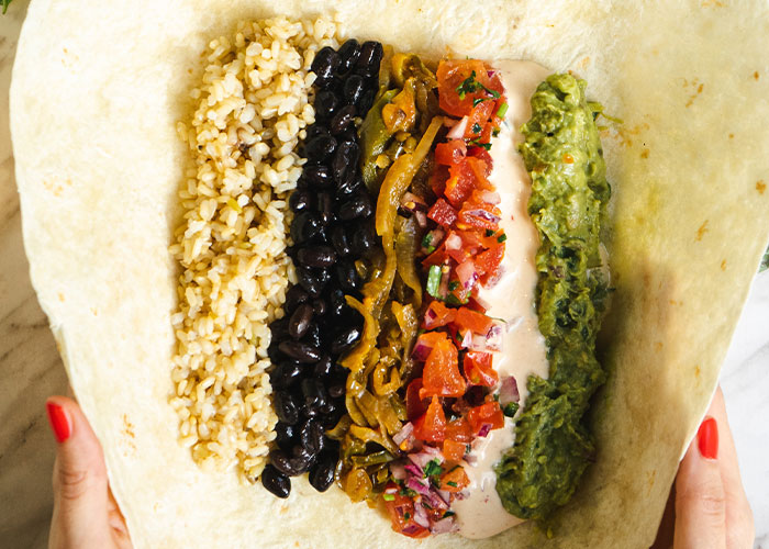 Close-up of a restaurant green flags burrito with rice, black beans, peppers, salsa, sauce, and guacamole on a tortilla wrap.