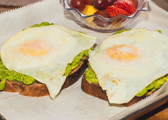Two slices of toast with avocado spread and fried eggs, highlighting restaurant green flags for quality food.