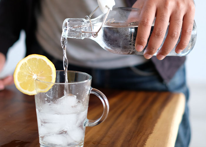 Person pouring water into a glass with ice and lemon, illustrating restaurant green flags for quality service.