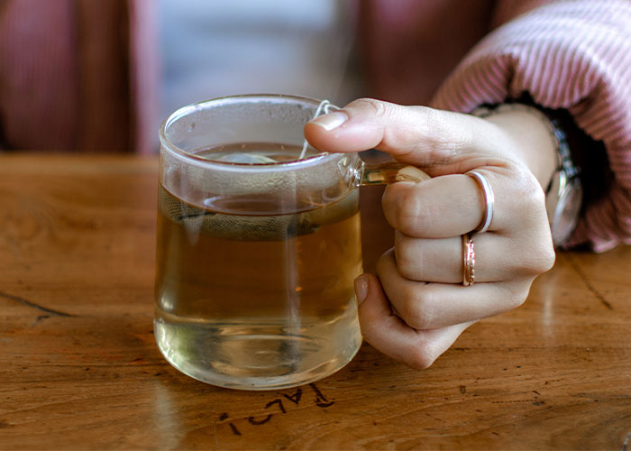 Hand holding a clear glass cup of tea on a wooden table, illustrating restaurant green flags for dining.
