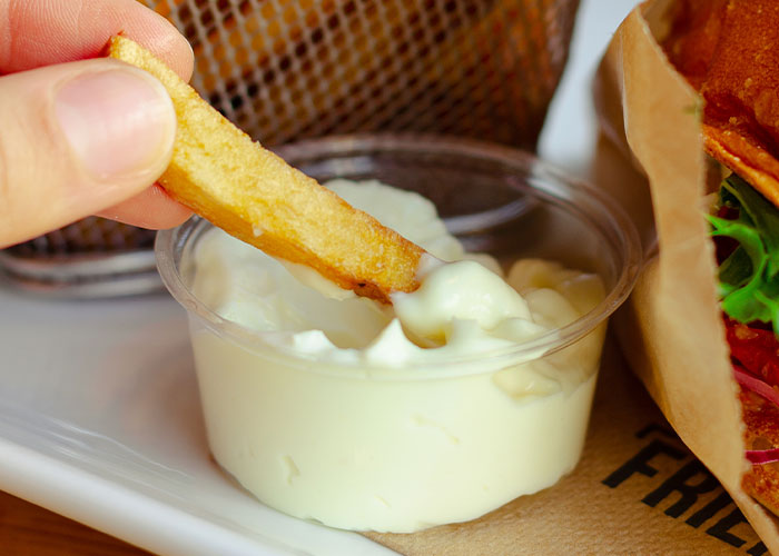 Close-up of a hand dipping a french fry into creamy sauce, illustrating restaurant green flags for a tasty meal.