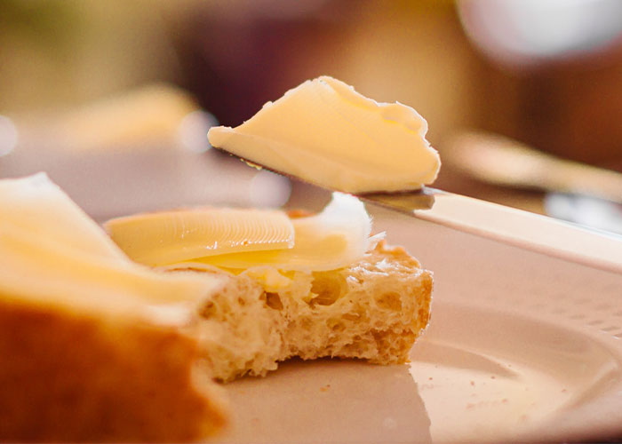 Close-up of fresh bread being spread with butter, highlighting restaurant green flags that indicate quality and taste.