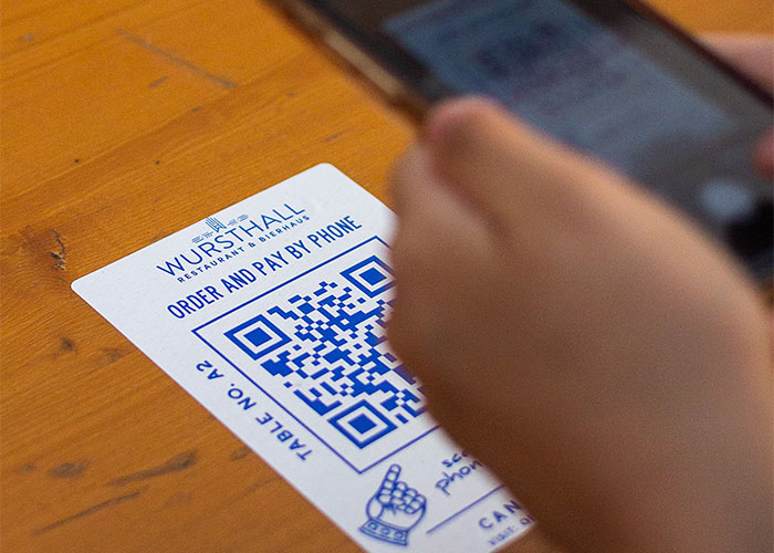 A person using their phone to scan a QR code for ordering, showing restaurant green flags and convenience.