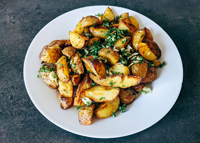 Roasted potatoes garnished with herbs on a white plate, illustrating restaurant green flags for quality food.