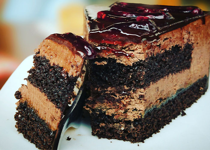 Chocolate layered cake slice with glossy chocolate topping on a white plate, indicating restaurant green flags for quality.