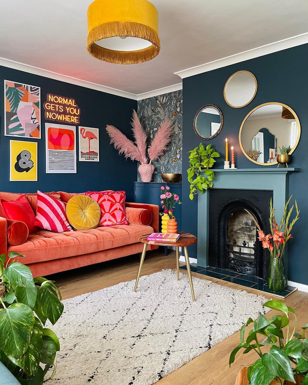 Colorful living room ideas featuring an orange velvet sofa, dark blue walls, and a decorative fireplace with mirrors.