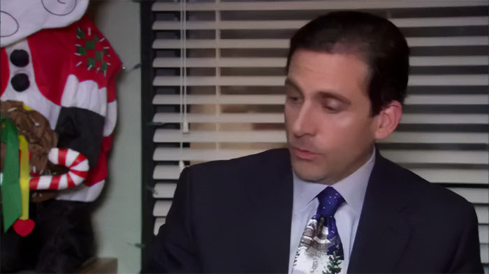 Michael Scott talking in an office setting, dressed in a suit and festive tie, showing leadership as the best boss ever