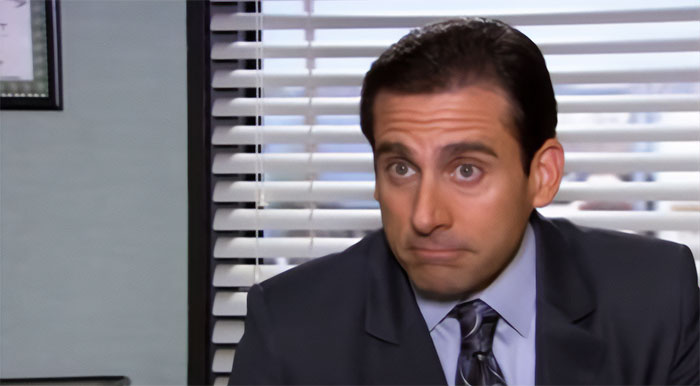 Michael Scott speaking in a suit with blinds in the background, showcasing iconic boss quotes from the popular TV series.