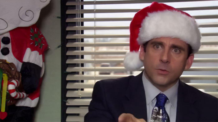 Michael Scott wearing a Santa hat and suit, speaking in an office setting, showcasing his best boss personality.