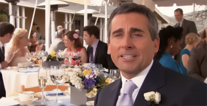 Michael Scott sitting at a wedding table smiling in a suit and tie, showcasing the best boss ever vibe.